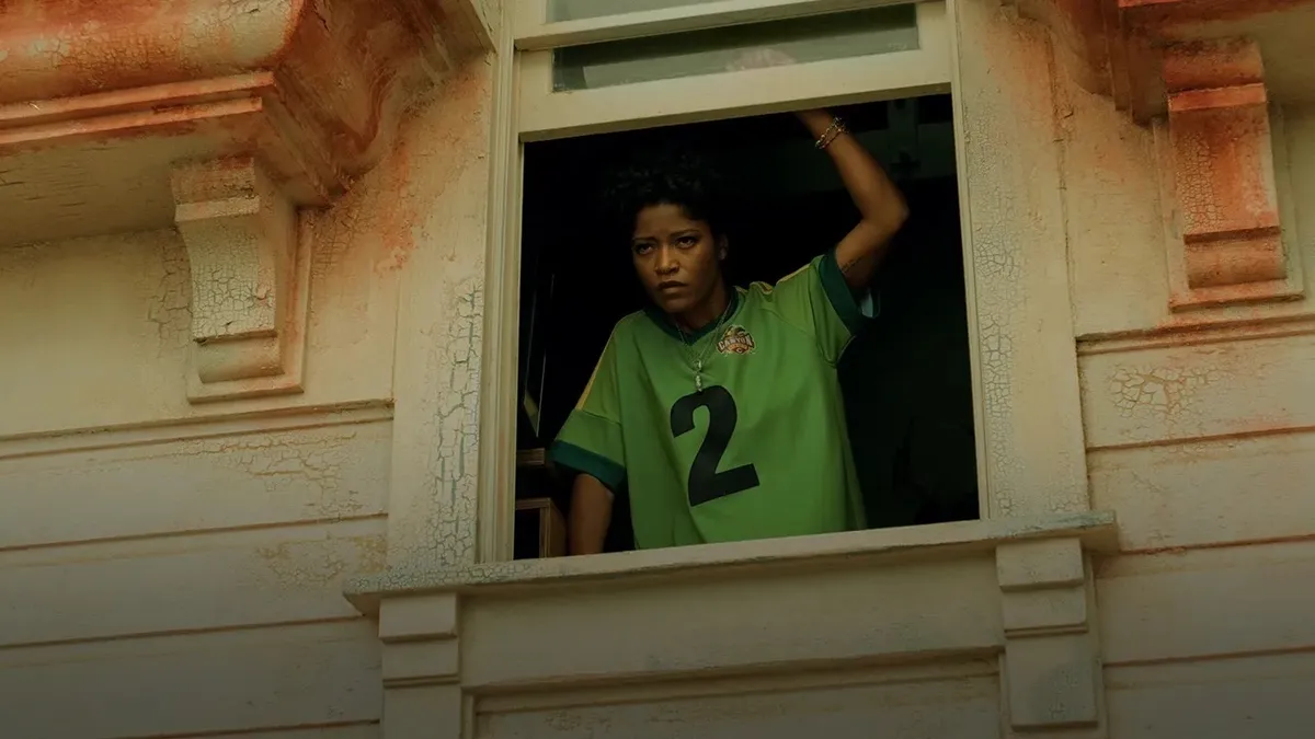 bathroom breaks during nope. black woman in a green jersey with number 2 on it looking out an open upstairs window.