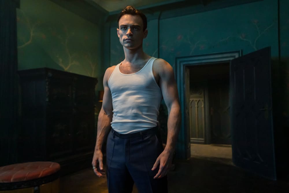 Is The Invitation (2022) bathroom breaks guide. Man in a white white beater tank top and pants standing in a room.