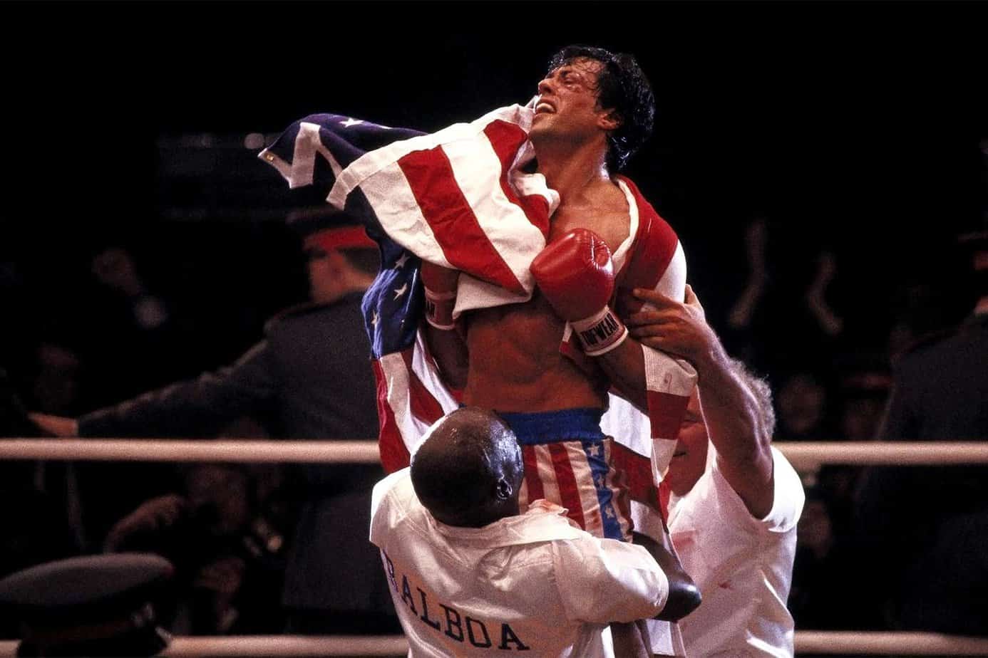 rocky movies to watch before creed III. Rocky 4 finale boxer wrapped in a US flag held up by two people.