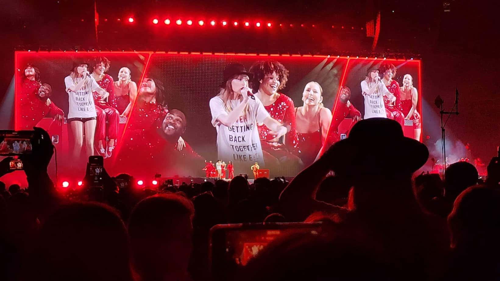 Taylor Swift singing 22 at the Eras Tour. Wearing a black hat and a shirt that says Never Getting Back Together. 